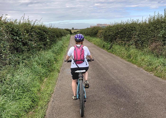 Woman cycling towards Bamburgh Castle Northumberland